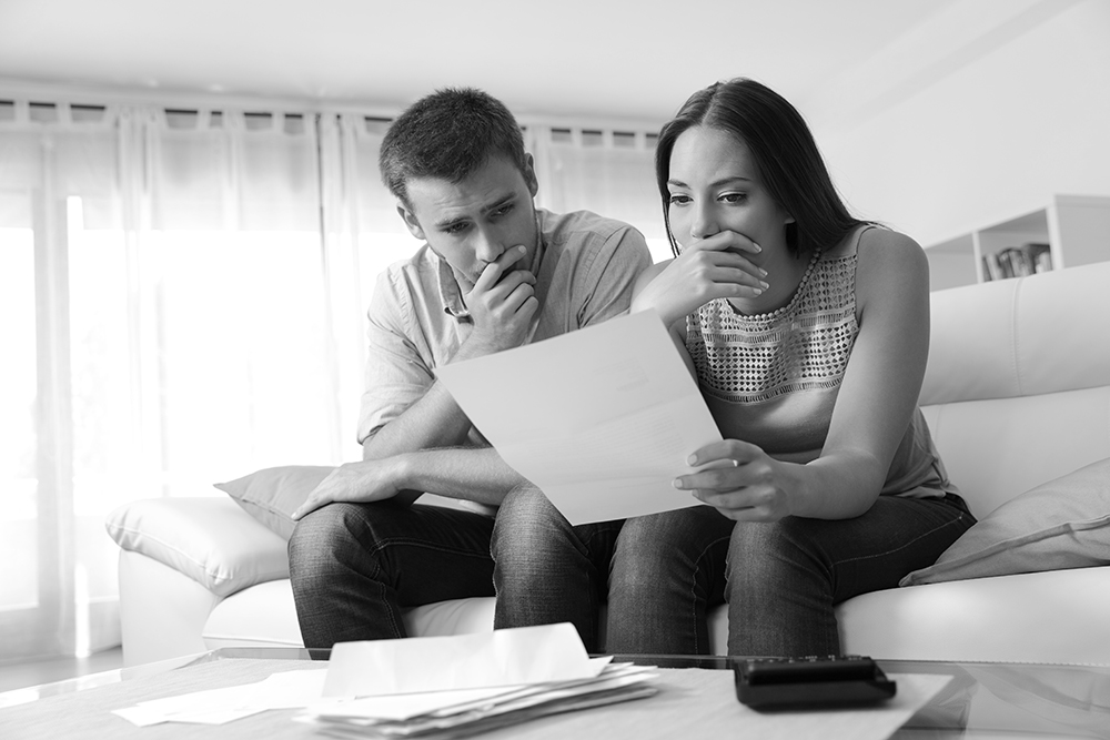 Worried couple reading a letter sitting on a couch in the living room at home
