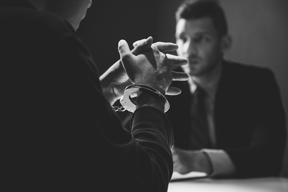 Criminal man with handcuffs being interviewed in interrogation room after committed a crime